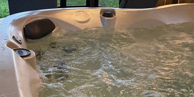 Indoor hot tub with a view of a lake and garden through large windows.