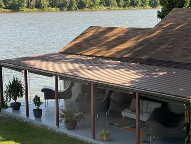 Covered patio with seating overlooking a calm river and trees.