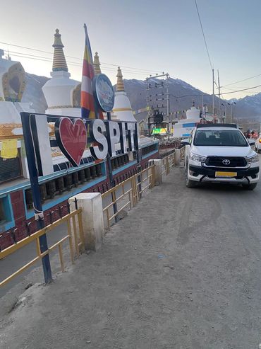 I love Spiti sign near Buddhist stupas and a parked white Toyota car.