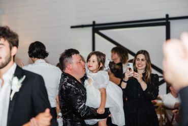 Officiant holding a flower girl during a DFW wedding reception, guests celebrating in the background