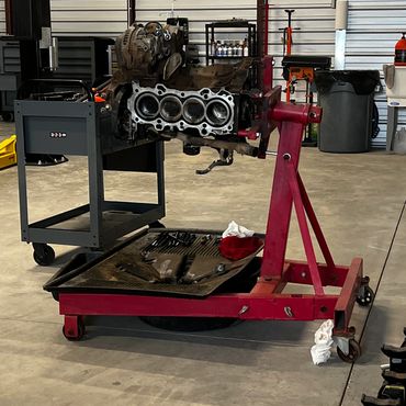 Automotive engine block mounted on a red engine stand in a workshop.