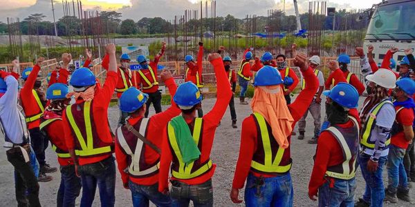 Construction workers in safety gear raising fists in unity at a construction site.