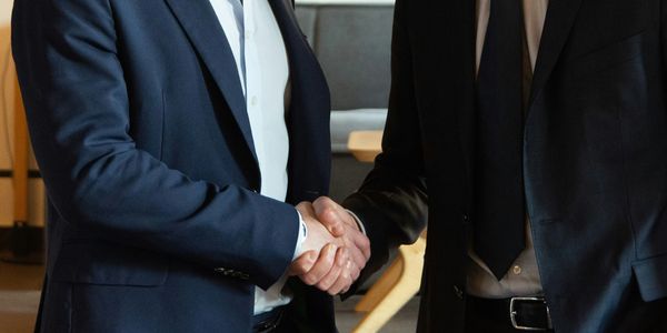 Two businessmen in suits shaking hands in an office setting.