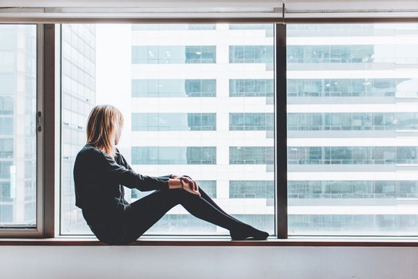 Mujer joven sentada en un ventanal, luz de día, ventana panorámica,