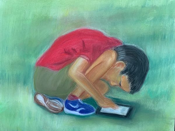 Young boy hunched over iPad on grass in park.