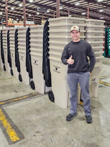 Man giving thumbs up beside lined-up trash bins in warehouse.