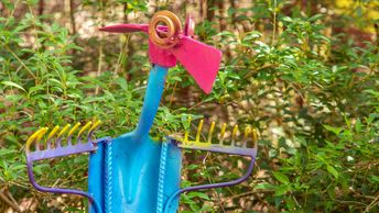 Colorful garden tools painted to resemble a bird among green foliage.