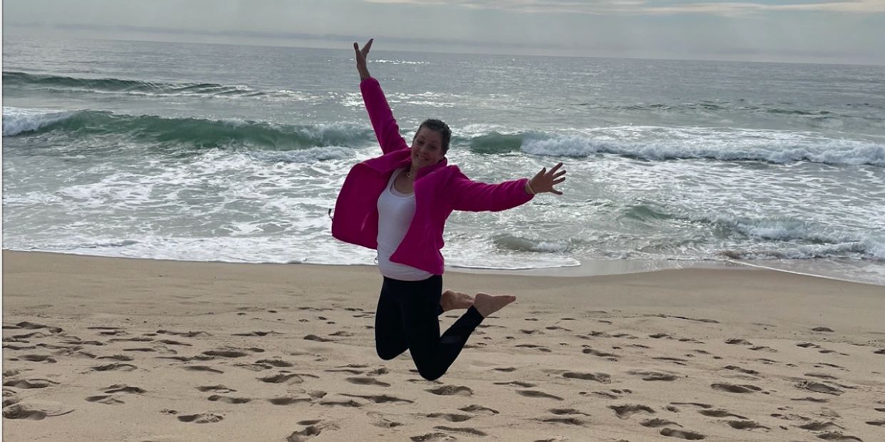 Person jumping joyfully on the beach near the ocean.
