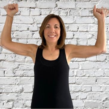 Woman in black tank top flexing her arms, smiling.