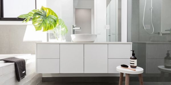 Modern white bathroom vanity with green plant and stool holding toiletries.