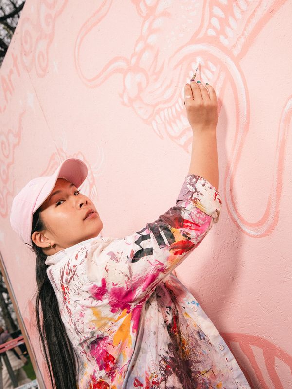 Artist painting a dragon on a pink wall.