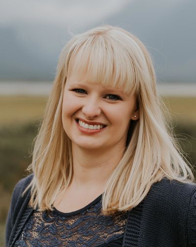 Smiling blonde woman with bangs outdoors.