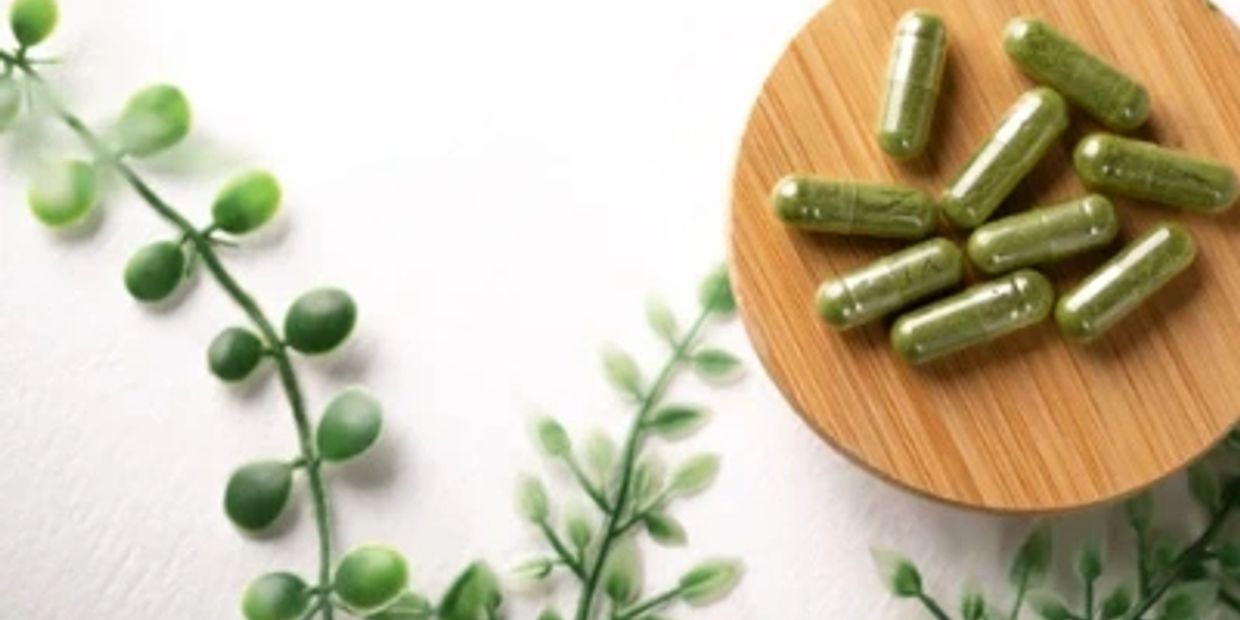 Green herbal capsules on a bamboo plate with greenery.