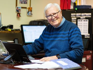 Smiling older man working at a desk with a laptop and papers.