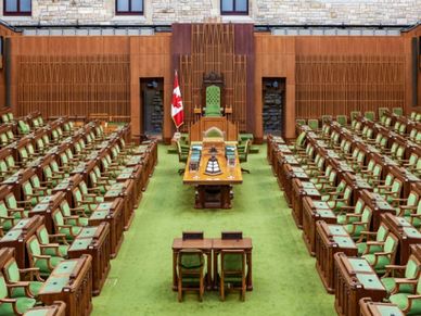 Empty parliamentary chamber with green seats and a Canadian flag.