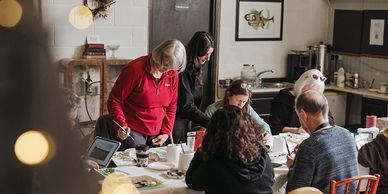Art students gathered around a table with art teacher. Paintings on table.