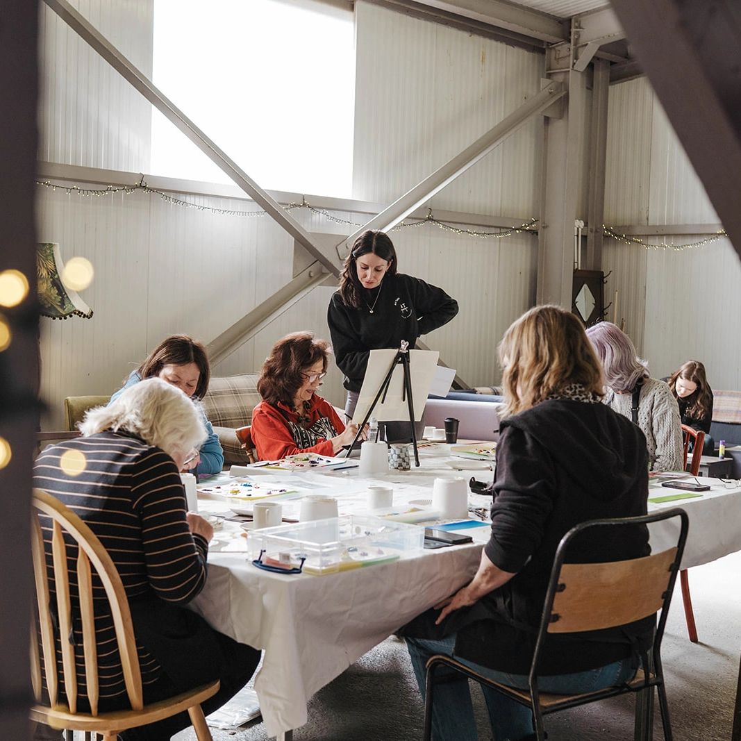 Students gathered around the table in the Old Brewery. Art Easel up and water jars and paint.