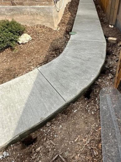 Newly poured concrete sidewalk with a curved design in a garden area.
