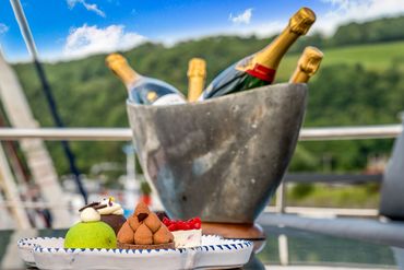 Assorted desserts on a plate with champagne bottles chilling in an ice bucket outdoors.
