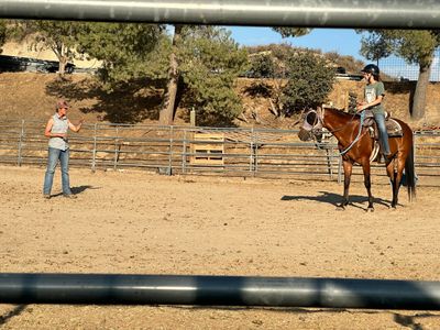 A person riding a horse is being guided by an instructor in an outdoor arena.