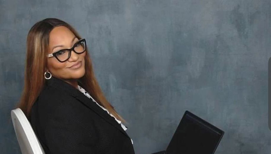 Woman with glasses sitting on a chair holding a laptop, smiling.