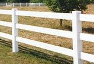 White vinyl ranch style fence along a grassy field with trees in the background.