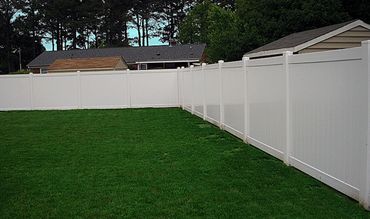 A backyard with a white vinyl fence and fresh sod