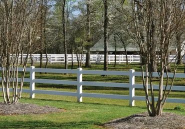 White horizontal rail fence in a field with trees.