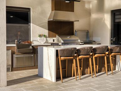 Custom outdoor kitchen with stone island, grill, and seating built by Patio Empire.