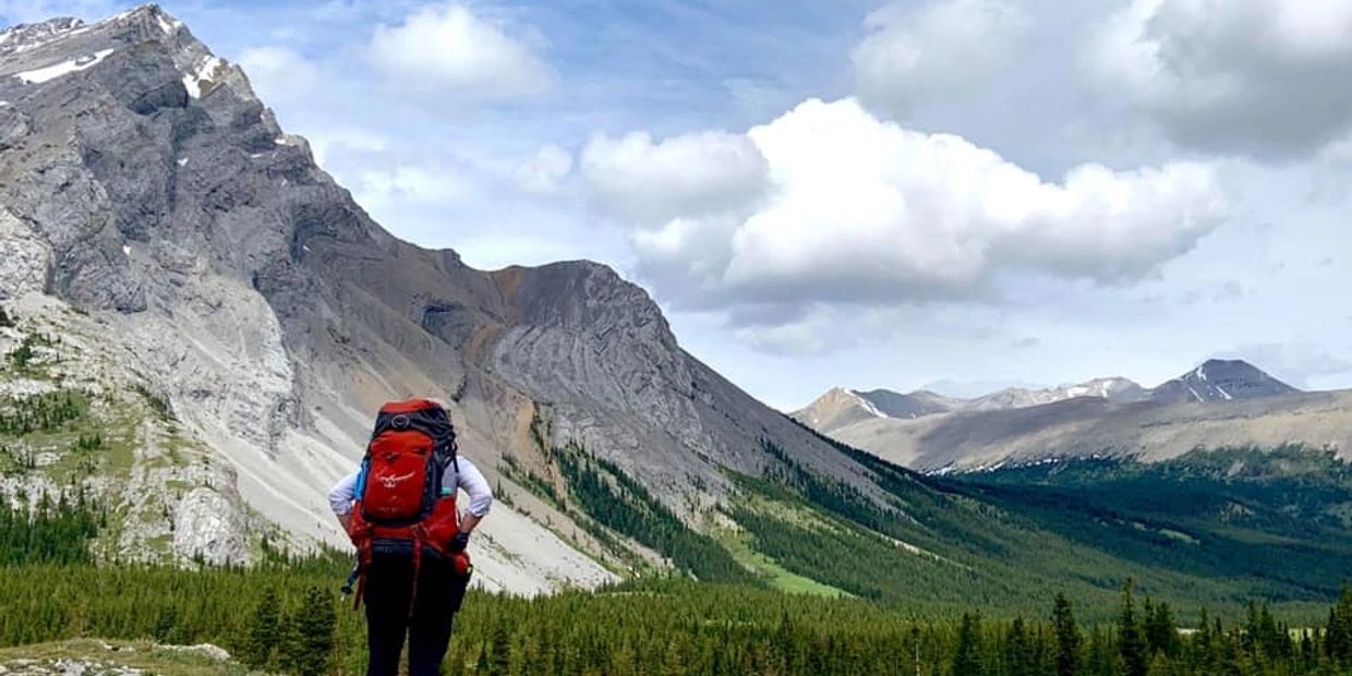 Hiker with a red backpack enjoying a mountainous landscape under a partly cloudy sky.
