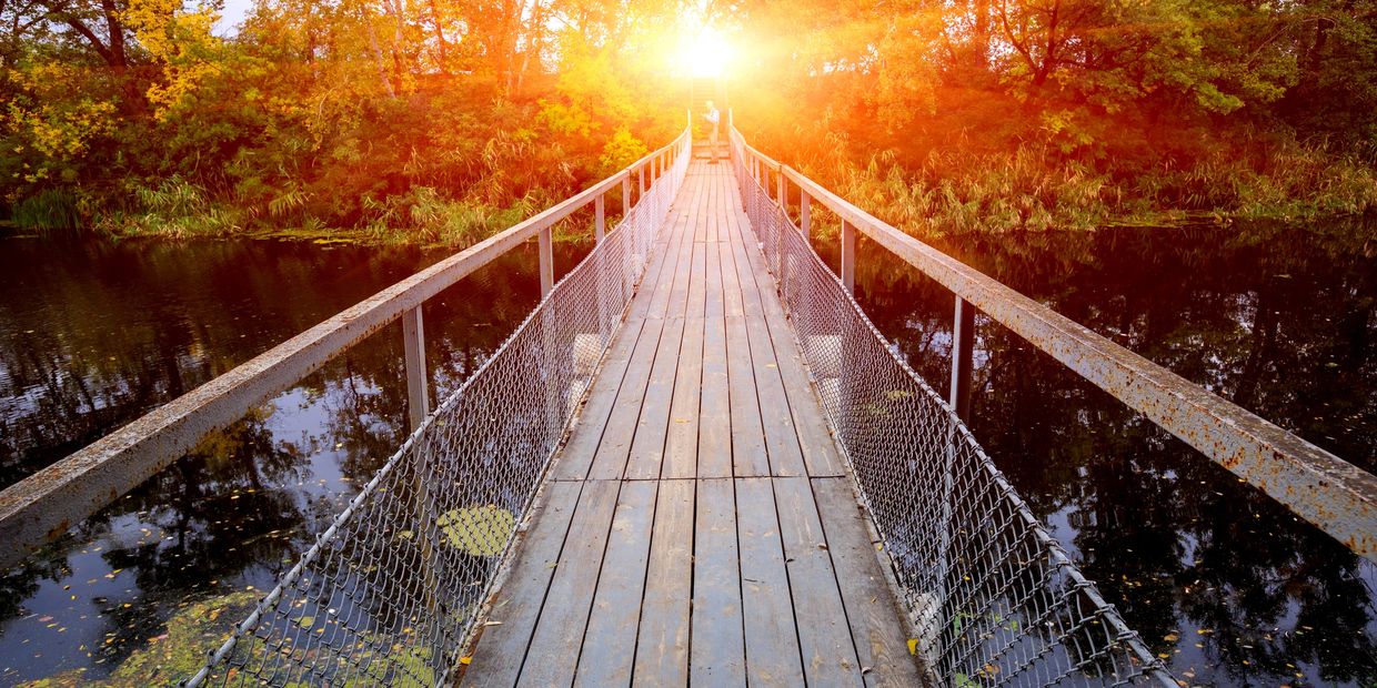 wooden bridge over a river with the sunrise in the background
