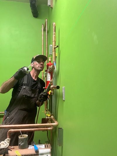 Plumber working on copper pipes against a green wall.