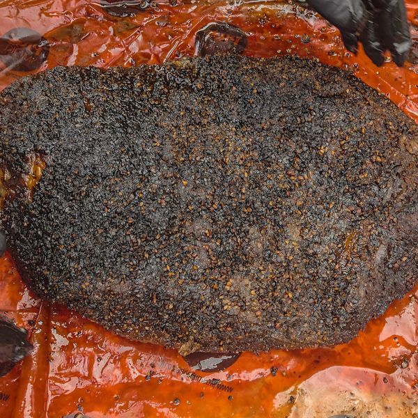 Smoked brisket with a dark, peppery bark on an orange surface.
