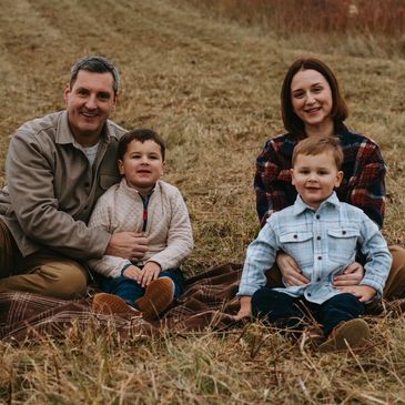A happy family of four sitting on a blanket outdoors in a grassy field.
