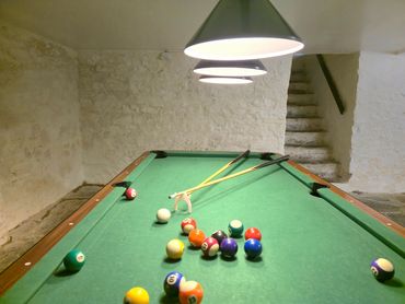 Hanging light giving lovely brightness over the pool table, cue and balls in mid play.