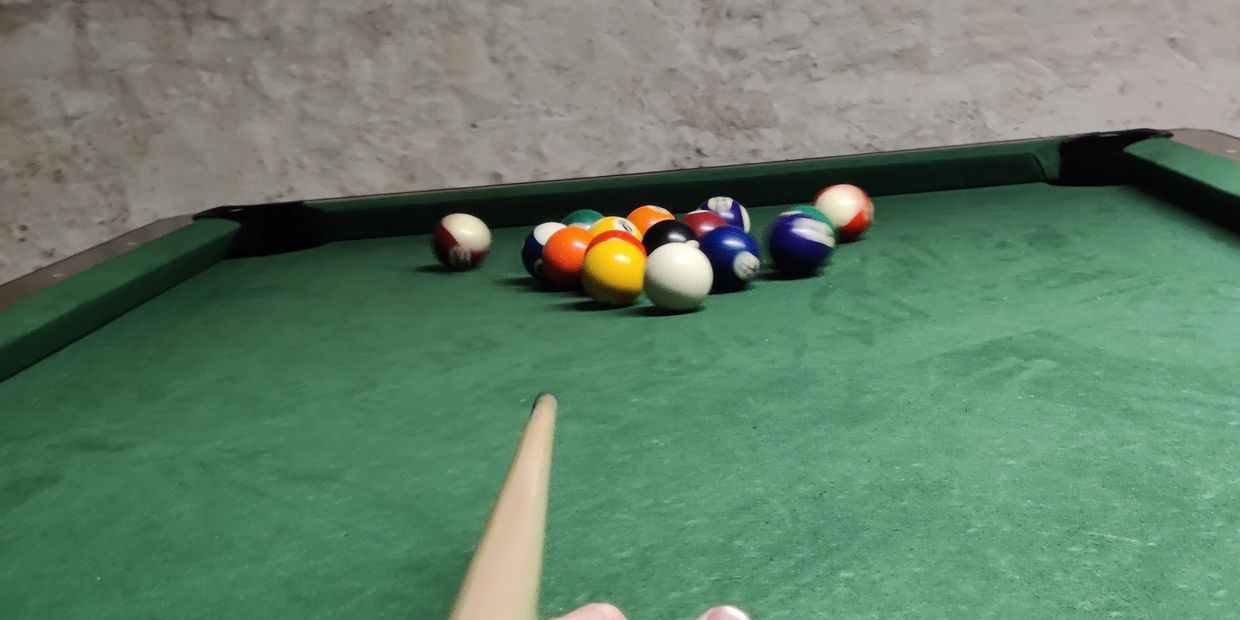 Action shot of a person with a cue having taken a shot and pool balls scattered over the table.