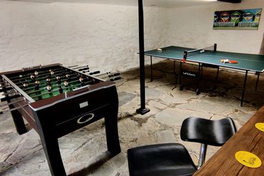 Cellar with a bar table and two stools looking out onto the football table and table tennis.