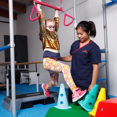 Kid with disability swinging on trapeze during intensive physiotherapy with physiotherapist