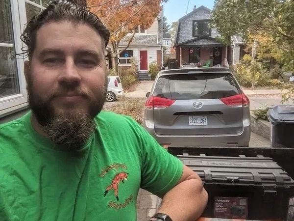 Man in green shirt with a beard taking a selfie outdoors in autumn near a parked minivan.