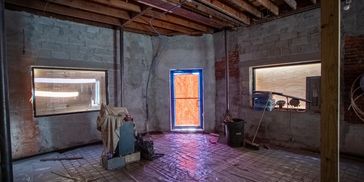Construction site interior with exposed ceiling and plastic-covered floor.