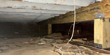 Crawl space with wooden beams and scattered debris on dirt floor.