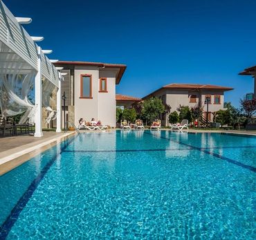 A clear blue swimming pool with people relaxing on lounge chairs under a bright sky.