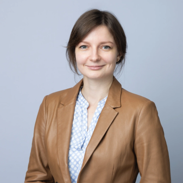 Professional woman in brown blazer smiles at the camera.