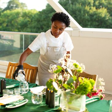 Person pouring water into a glass at a beautifully set outdoor table.