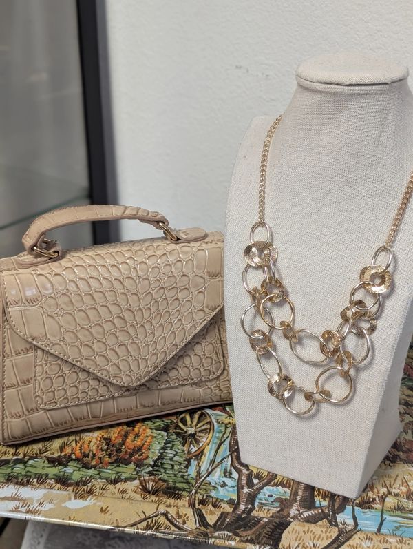 Tan purse, gold tone necklace displayed on a vintage tray