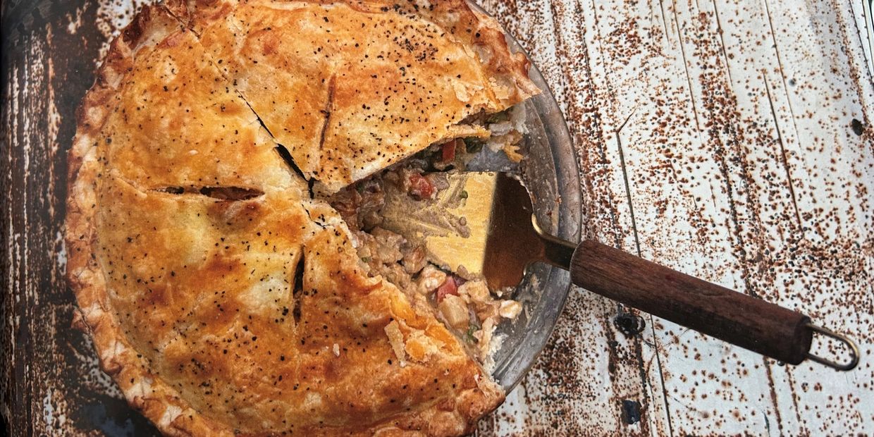 A homemade chicken pot pie with a golden crust and a slice being served.