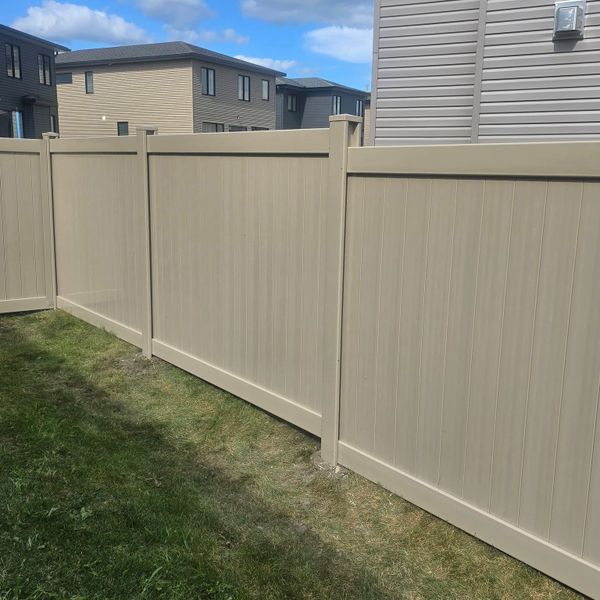Beige vinyl privacy fence enclosing a grassy backyard in a suburban neighborhood.