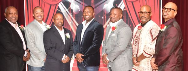 Group of seven men dressed formally posing indoors.