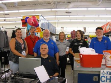 Group of seven people, including police and community members, smiling indoors at a booth.