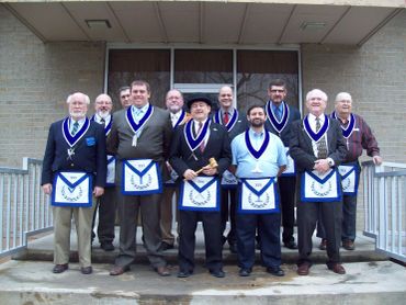 Group of men in Masonic regalia standing on steps outside a building.